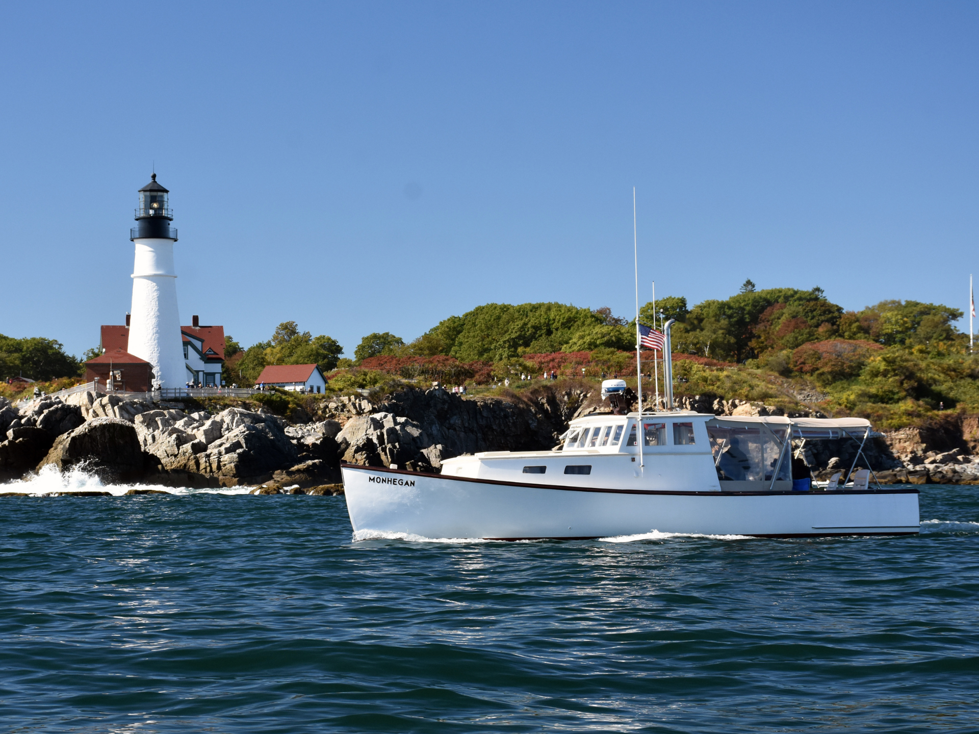 Restored lobster boat the Monhegan passing by Portland Headlight on a sunny day.