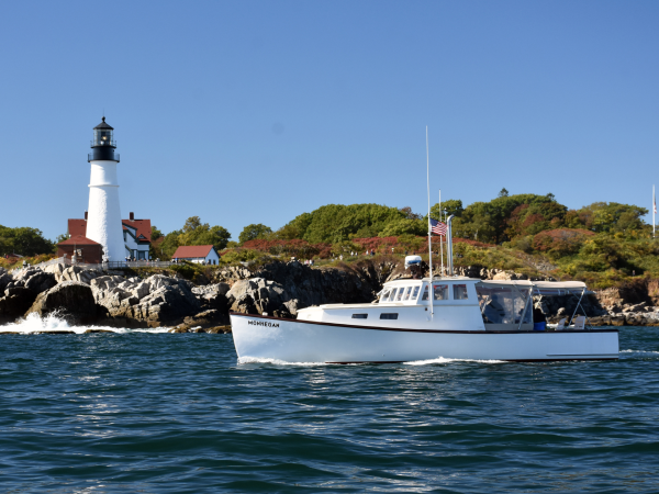 Restored lobster boat the Monhegan passing by Portland Headlight on a sunny day.