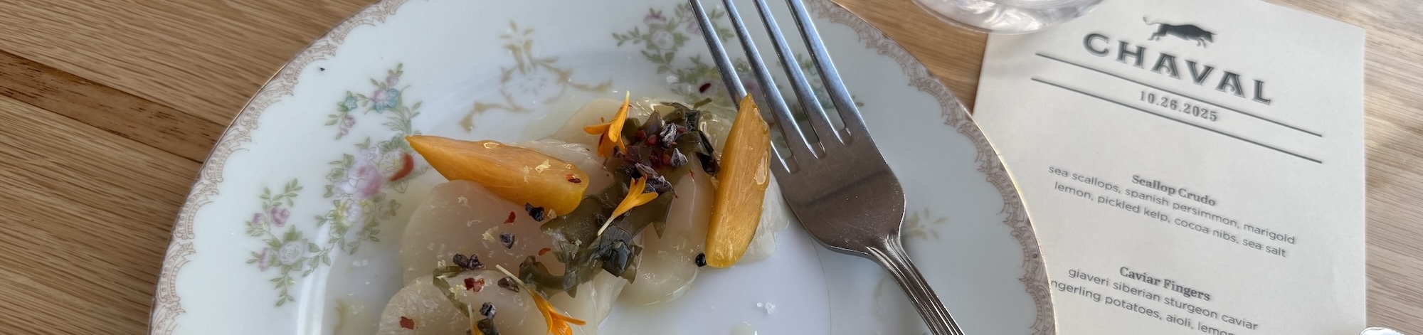Gourmet dish with fork, menu, and decorative plate on a wooden table.
